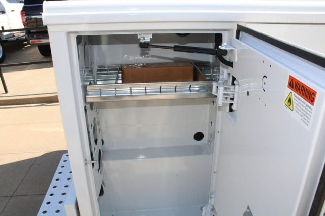 Ford F-250 service body with open storage compartment showing interior shelves and warning label on door.