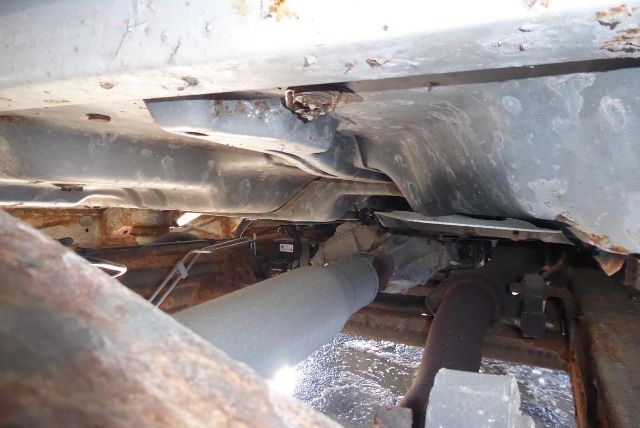 Underneath a 2011 Chevrolet 2500HD showing drive shaft and suspension components with rust and dirt, visible exhaust pipe and chassis framing.