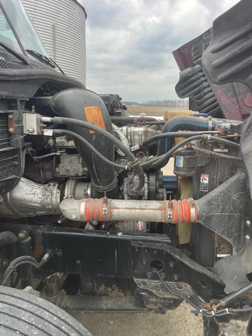 Engine bay of a Freightliner Cascadia with visible air intake hose, radiator, hoses, and a front crossbar; includes coolant reservoir and engine components.