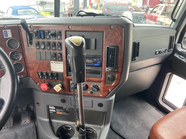 Truck cab interior showing dashboard with numerous switches, woodgrain panels, and a gear shifter. Visible text includes labels on switches and a small warning label.