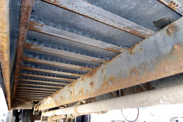 Underbody view of a Freightliner FS65 bus chassis showing rusted I-beam frame rails and drivetrain components.