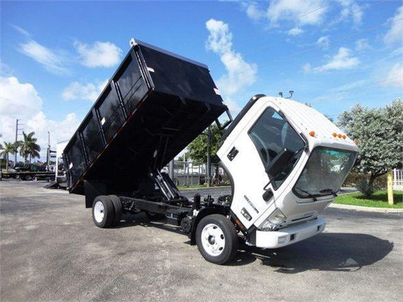 Isuzu NPR HD dump truck in service position with cargo bed raised, white cab, black dump bed, roadside lot.
