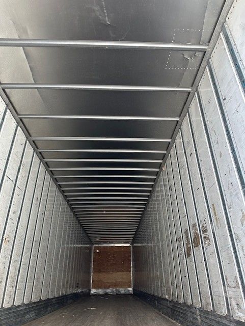 Interior of a utility trailer cargo area with metal walls and ceiling ribs, long narrow perspective toward front.