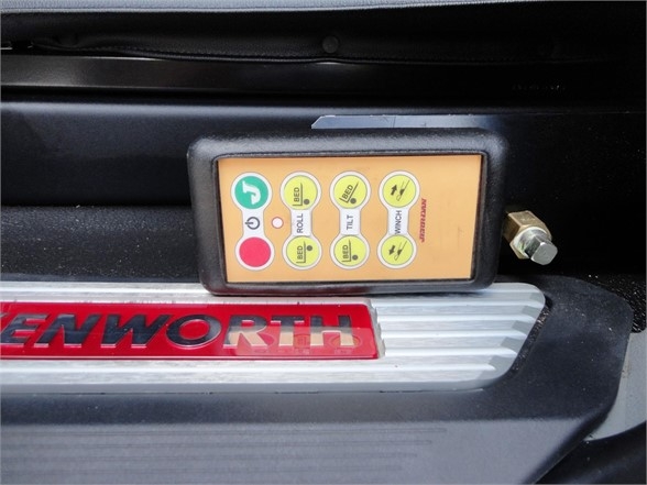 Kenworth W990 truck showing a control pendant with labeled buttons and a red Kenworth logo plate below.
