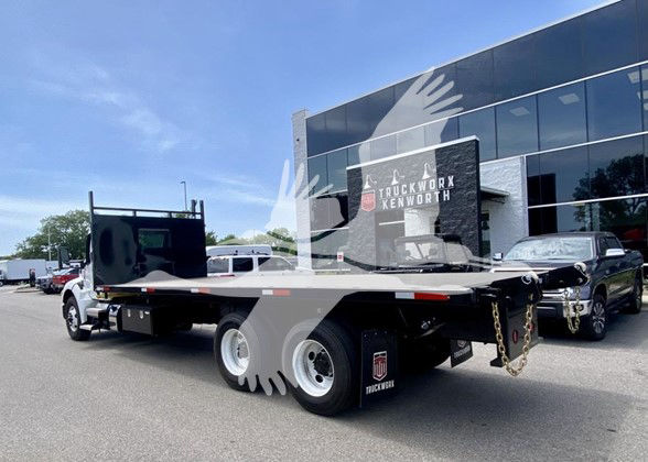 Kenworth T480 flatbed truck in dealership lot, rear view showing flatbed with dual rear wheels and chrome accents.