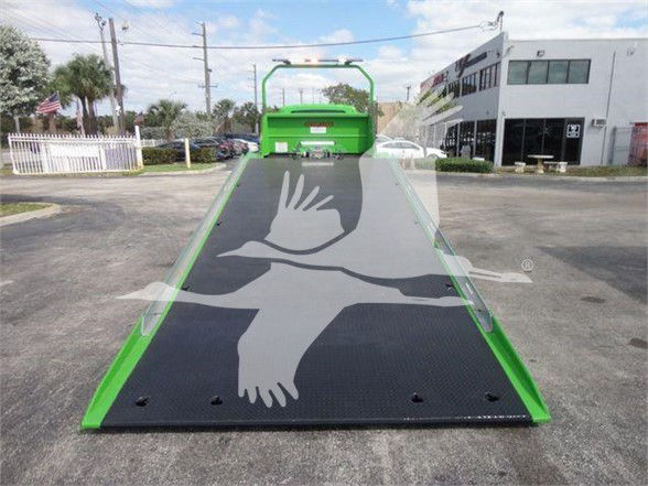 Green International MV tow truck with a fold-down ramp and black textured platform/overlay for loading, seen from the rear in a dealership lot.