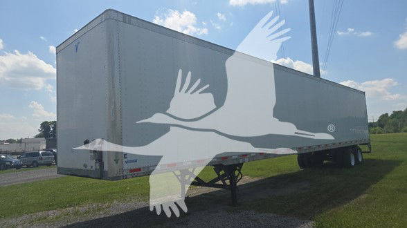 Trailer with side box showing Vanguard logo overlay, long rectangular cargo trailer on legs in a grassy lot.