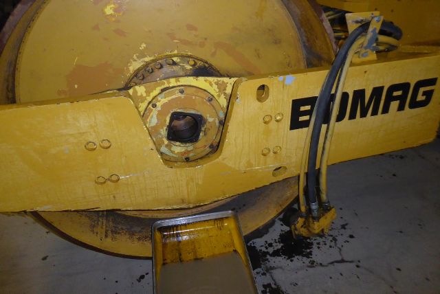 Bomag BW212D-2 drum roller showing hydraulic hose and front drum assembly with yellow paint and EMAG branding partially visible.