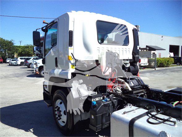 Isuzu FTR cab forward truck front-left view with engine components and fluid reservoirs visible in daylight.