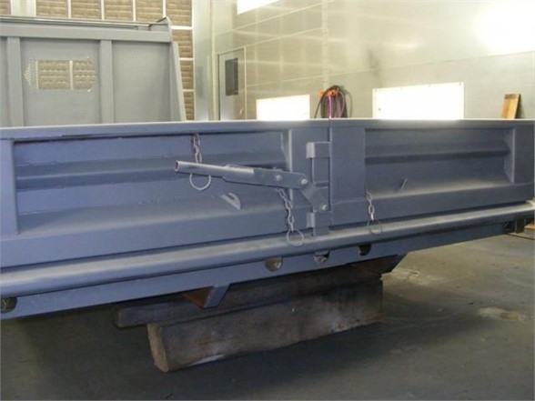 Blue dump body side rail with latch and chains attached, situated in a workshop.