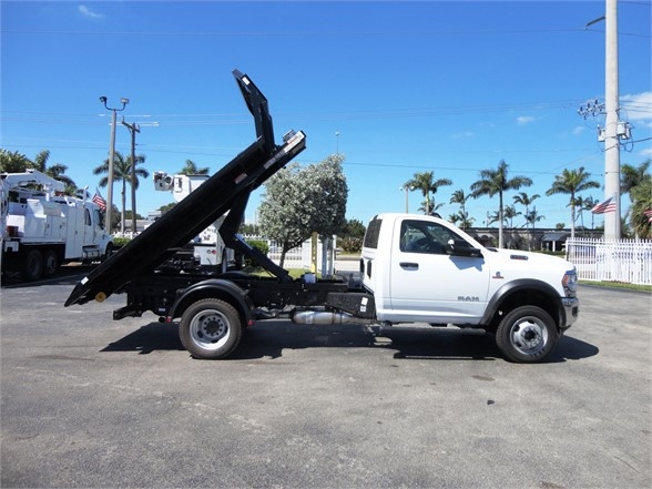 2023 Ram 5500 HD white cab with black hooklift body, side view showing hoisted dumping area and truck chassis.
