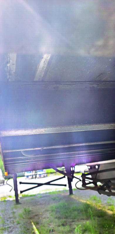 Trailer underside and frame with dark side panels, support legs and wheel area visible. Narrow view shows structural cross members and stabilizer legs.