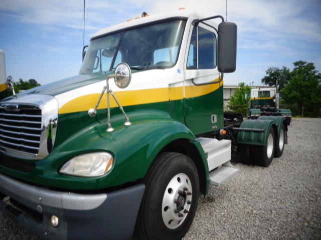 Freightliner Columbia truck cab with green and yellow stripe, front fender, large side mirror, and dual rear wheels; visible grille and headlight.