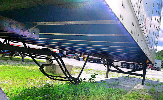 Underneath view of a Vanguard VXP trailer showing suspension and wiring; blue-painted bottom exterior with support legs visible.