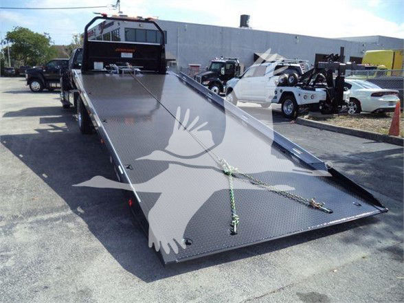Flatbed tow truck bed with Diamond plate surface, rear ramp lowered, Ford F-750 XLT stock number F750CRWCAB22XLPFM in a dealership lot.