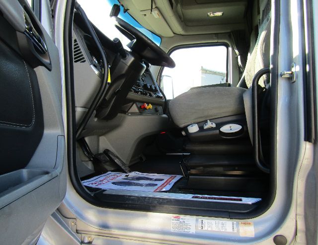 Truck cab interior view of a Kenworth T680 single cab showing steering wheel, dashboard, driver seat, and open door.