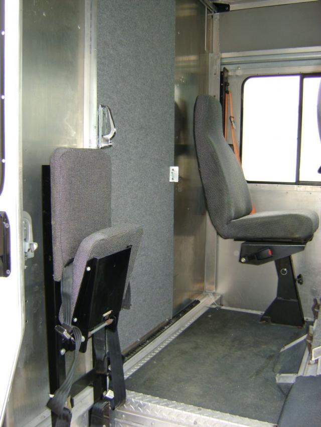 Cab interior of a Freightliner MT45 step van showing grey fabric seats, a partition panel, and metal framework.