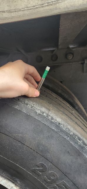 Trailer wheel well showing a hand holding a small green-tipped pencil-like object near the tire on a 2014 Wabash dry van trailer.