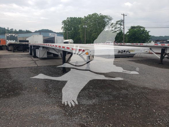 Flatbed trailer showing chrome frame and sidelight markers, with other trailers in background.