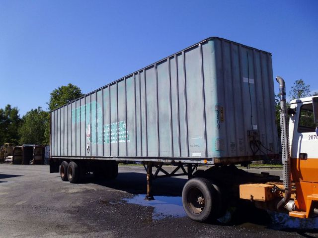 Fruehauf F69-F2-45 box trailer attached to a truck, side panels with vertical ribs, weathered grey-blue paint, two rear axles, support legs down, a small trailer wheel visible in foreground.