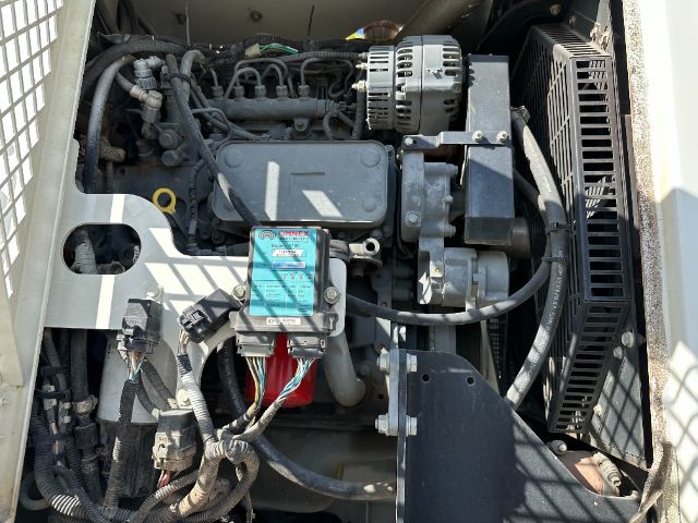 Engine bay of a 2009 International 7500 vacuum truck showing an air filter housing, alternator, belts, wiring, and a blue-fluid reservoir with labels.