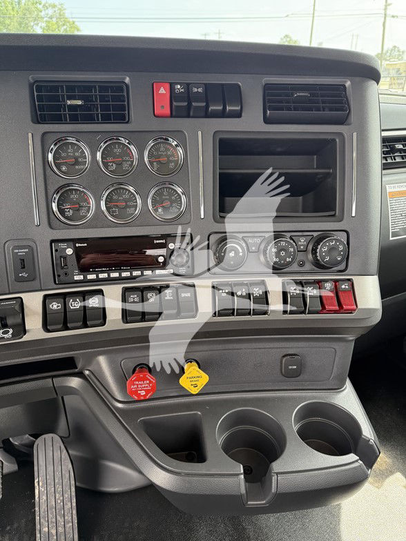 Kenworth T880 truck dashboard showing multiple gauges, controls, air vents, storage bin, cup holders, and two colored knobs (red and yellow) near lower panel.