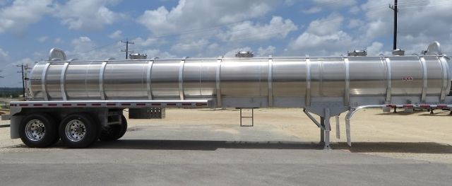Aluminum vacuum tank trailer on a long flatbed, cylindrical tank with ladder rungs and support wheels underneath.