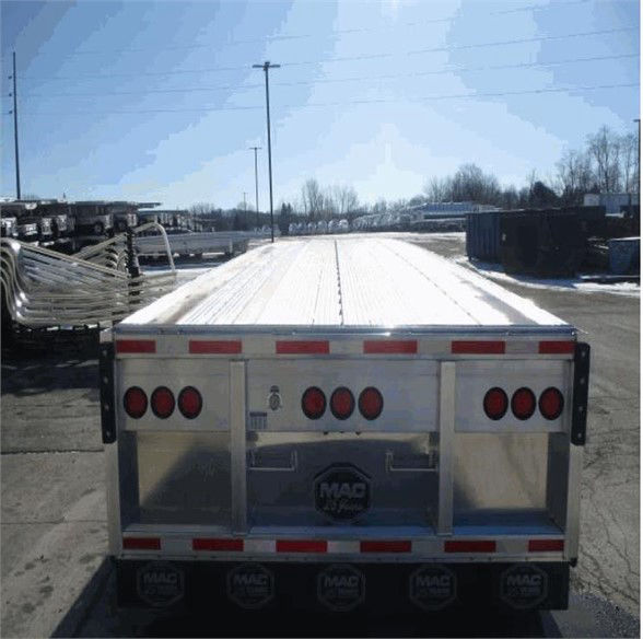 Tri-axle flatbed trailer rear view showing MAC bumper and multiple circular taillights.