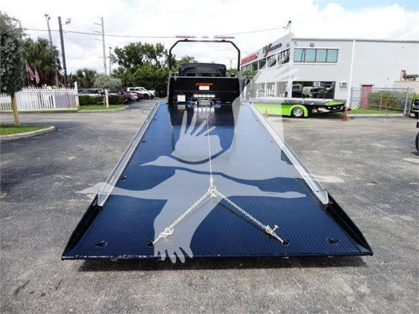 Photo of a 2022 Peterbilt 337 tow truck with a black flatbed, chains secured on the bed, and a dealership backdrop.