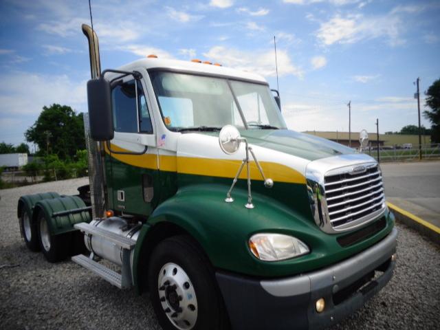 Truck cab showing Freightliner Columbia with green, white, and yellow livery, chrome grille, dual round mirrors, and large front bumper.