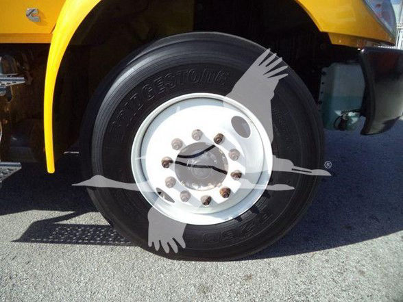 Tire and wheel of a yellow International DURASTAR 4300 truck. Wheel shows OEM steel rim with multiple lug nuts and tire with brand/model text partially visible. Vehicle fender and part of yellow cab visible.