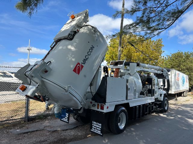 2009 International 7500 vacuum truck with a large rotating tank mounted on the back, tanker tip at an angle, VACON logo visible on the tank, side exhaust, equipment and hose housing, trailer hitch, and rear warning lights.