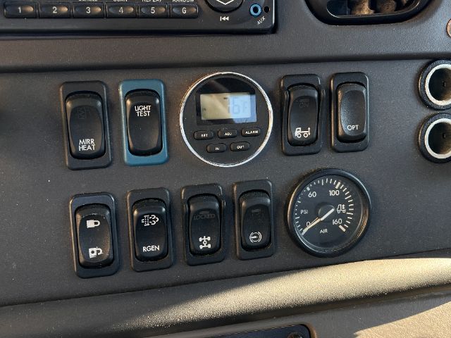 Freightliner M2 cab cluster with multiple switches and a round digital gauge; visible labels include MIRR HEAT, LIGHT TEST, RGEN, OPS, and a round gauge with PSI and degrees.