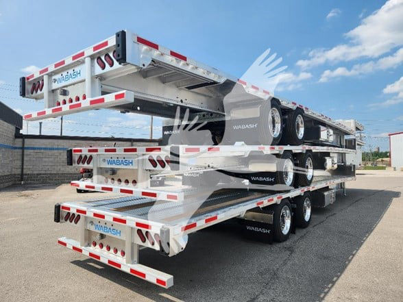 Wabash drop deck trailers stacked three high on a transport trailer; visible logos read 'WABASH' on ramps and sides; rear shows license plate area and taillights; stacked triple-axle trailers have black wheels and silver frame.