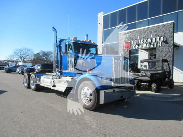 Kenworth W900L tractor-trailer in blue exterior with chrome accents parked outside dealership.