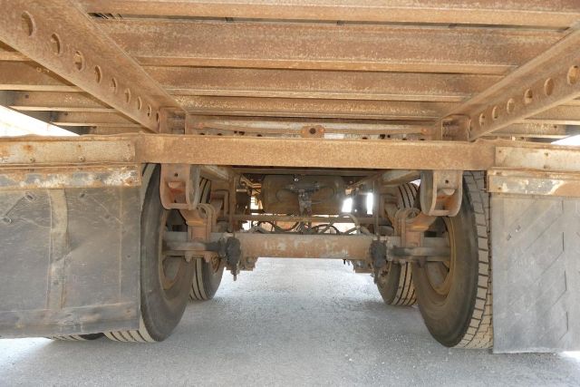 Trailer undercarriage showing dual rear axles and suspension components, rusty frame, and air reservoir visible between wheels.