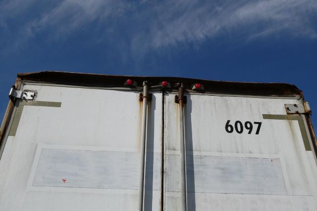 Rear of a white Fruehauf trailer with double doors, number 6097, rust on hinges and red marker lights at top.