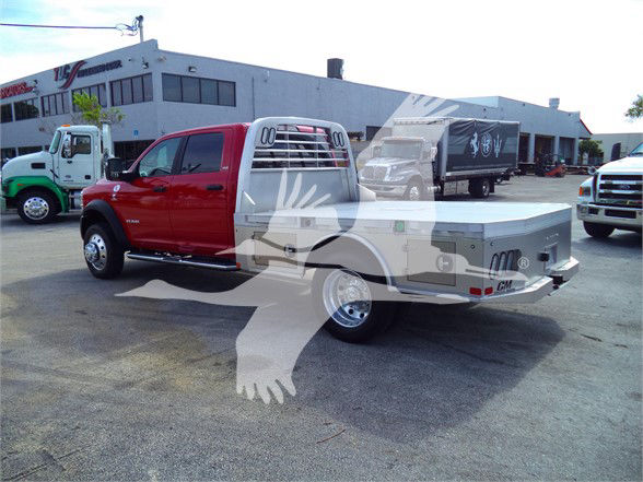 2023 Ram 5500 SLT flatbed truck with red cab and gray flatbed, parked in lot with other trucks.