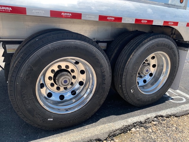 Dual axle aluminum end dump trailer with visible tires and rims, chrome wheels, and reflective red/white side markings.