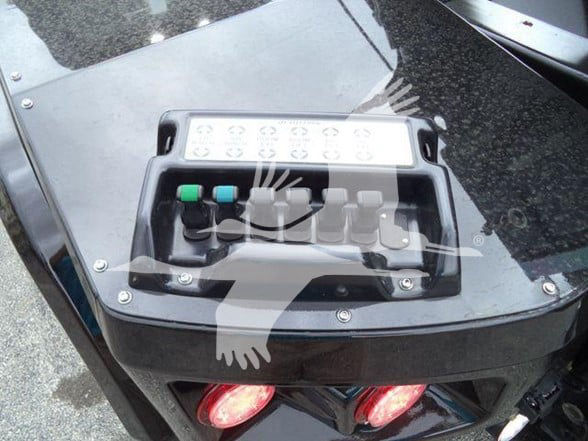 Tow truck chassis with control panel showing three colored levers and a row of circular buttons; glossy black surface with bolts and red taillights.