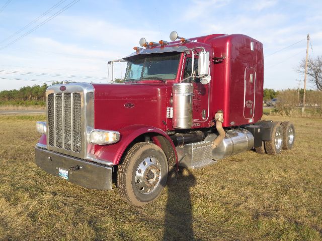 Peterbilt 388 conventional sleeper truck in a maroon color with chrome grille and dual rear axles, side view displaying fuel tanks and exhaust stacks.