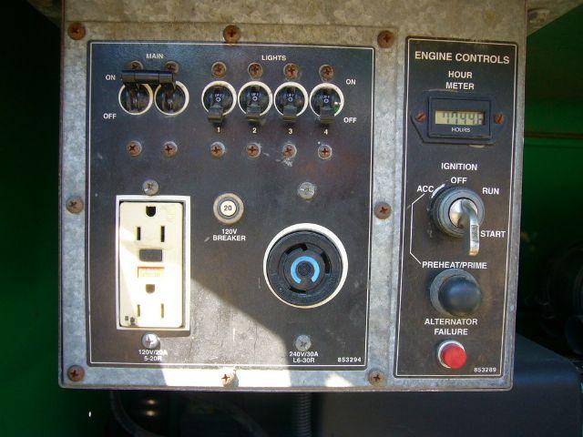 Truck equipment control panel with main switch, lights, engine controls, hour meter, ignition, and power outlet; circular blue start/stop switch and 120V outlet.