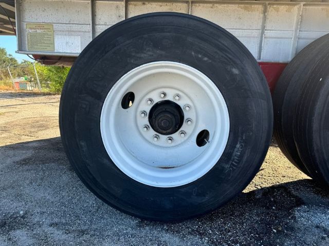 Wheel showing white steel rim with black tire on trailer axle, GMC trailer body in background.