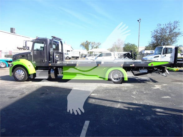 2022 Peterbilt 337 tow truck in green and black with low ride height, side view showing flatbed tow chassis and cab, no visible text on decals.