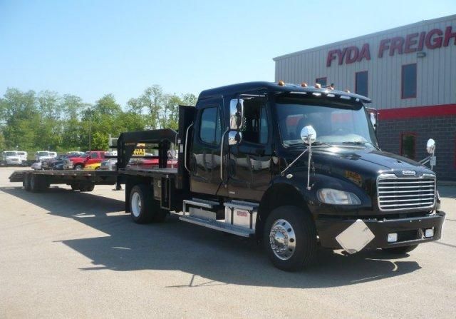 Flatbed tow truck with black cab and chrome accents parked in lot in front of Fyda Freight building.