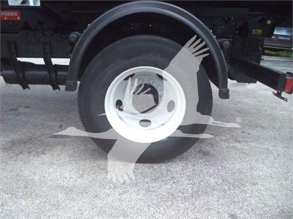 Wheel of a Freightliner BUSINESS CLASS M2 106 truck showing white steel wheel and tire with fender and undercarriage components.