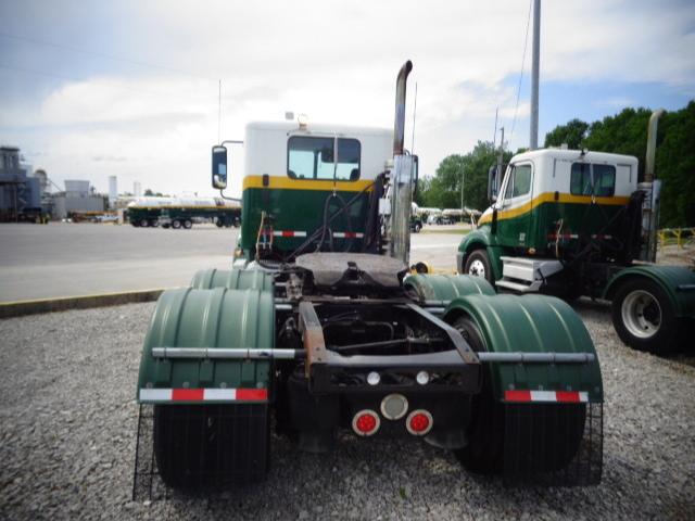 Truck tractor chassis and rear view showing fifth wheel and dual rear axles with mud flaps, green fenders, and white cab in background.