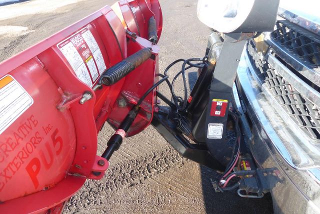 Front view of a 2011 Chevrolet 2500HD with a mounted red snow plow attachment connected to the vehicle's front hitch and wiring.