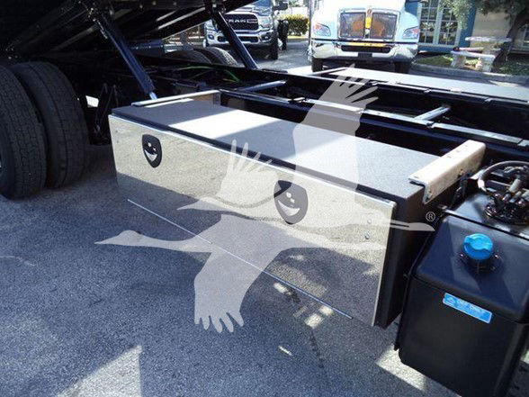 Truck bed toolbox mounted beside fuel tank in the International DURASTAR 4300 chassis cab. Visible components include a large rectangular metal toolbox with a pair of latches and a blue-capped fill/maintenance port nearby.