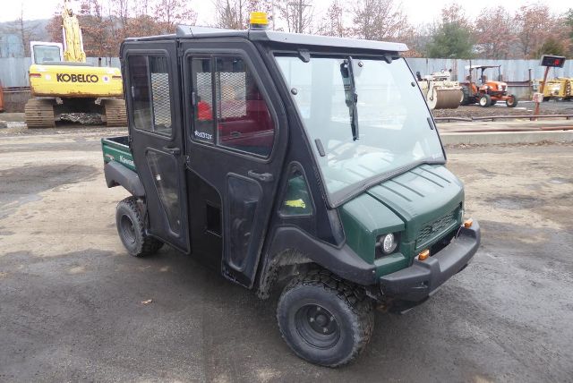 All-terrain utility vehicle with enclosed cabin and cargo bed, dark green body, front bumper, headlights, and windshield wipers visible.